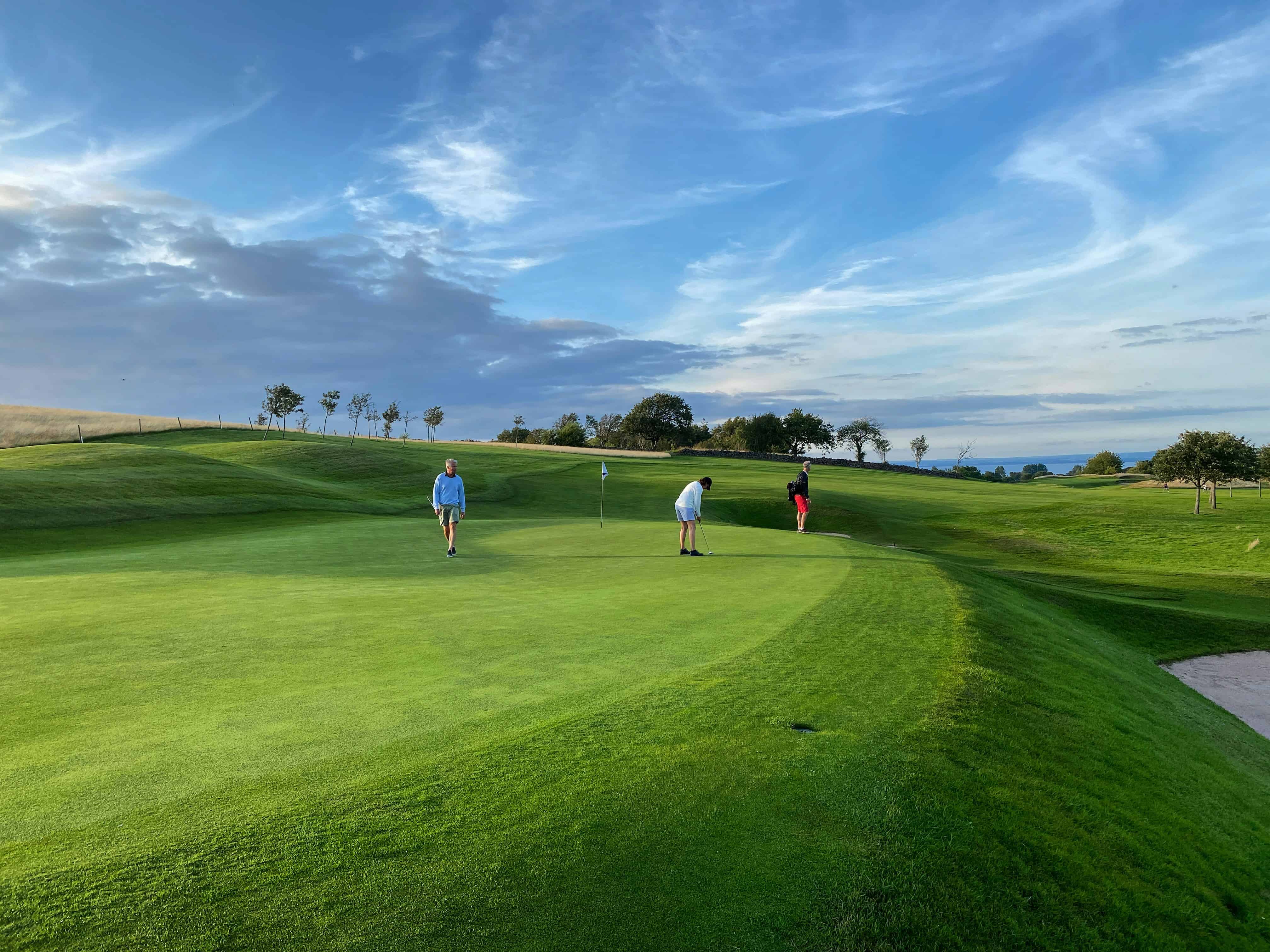 Golfers on a putting green with the coast in the distance