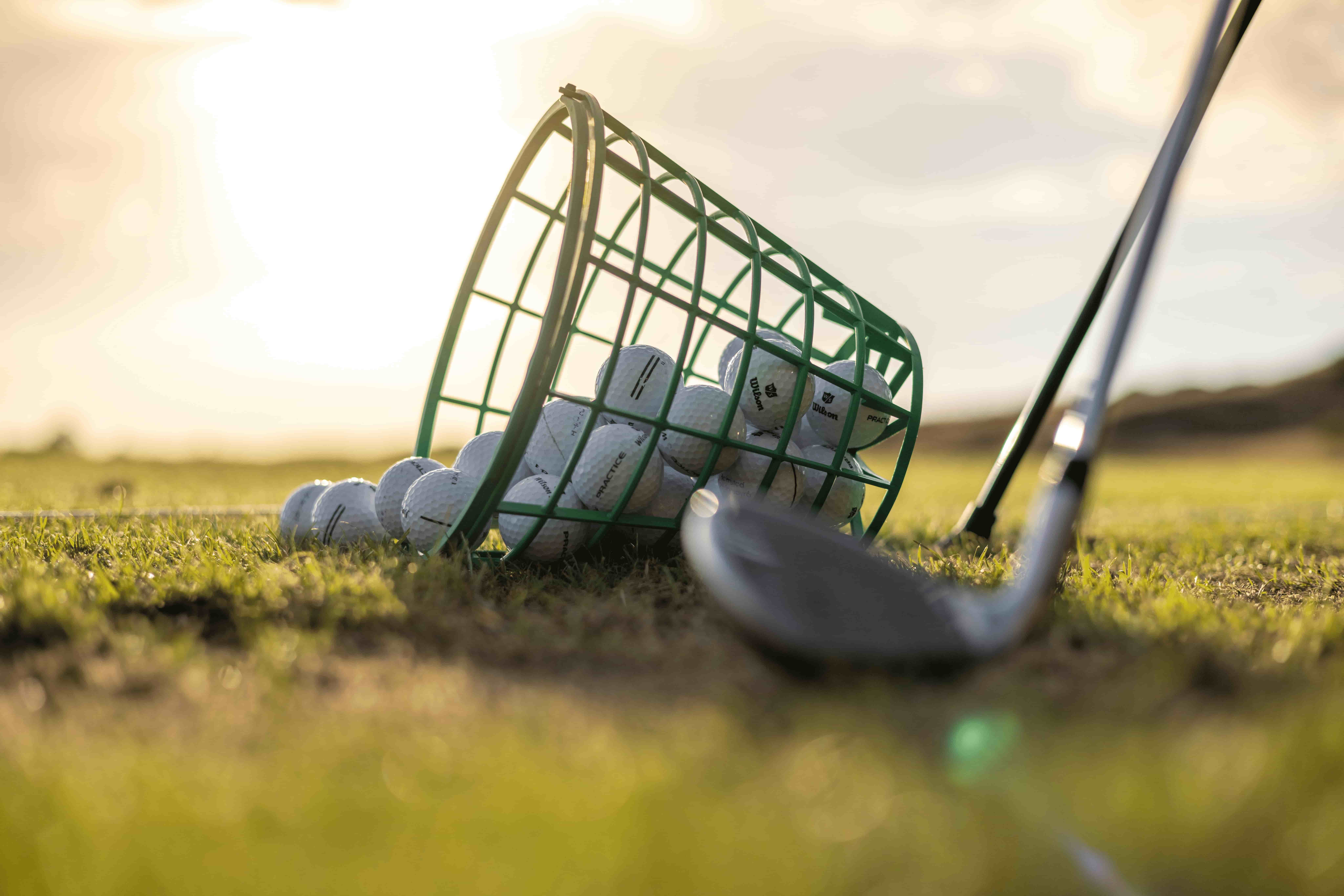 A bucket of golf balls tipped over beside a golf club on the grass